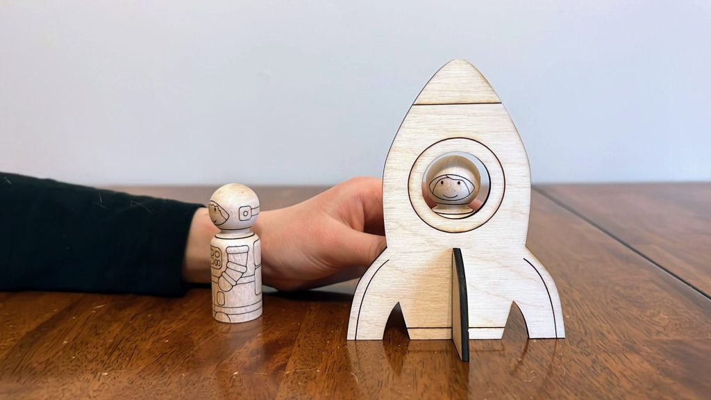 Wooden space ship and peg dolls being played with by a child.