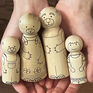 Small hands holding laser engraved peg dolls in the image of Goldilocks, Baby Bear, Papa Bear, and Mama Bear from Goldilocks and the Three Bears